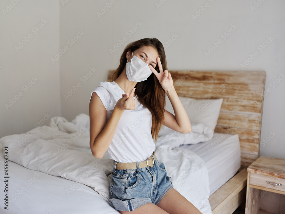 red-haired woman in a medical mask sits on the bed and gestures with her hands red-haired woman in a medical mask sits on the bed and gestures with her hands
