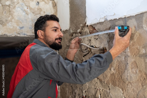 Plumber with tape measure measures the distance between pipes to avoid puncturing them when drilling photo