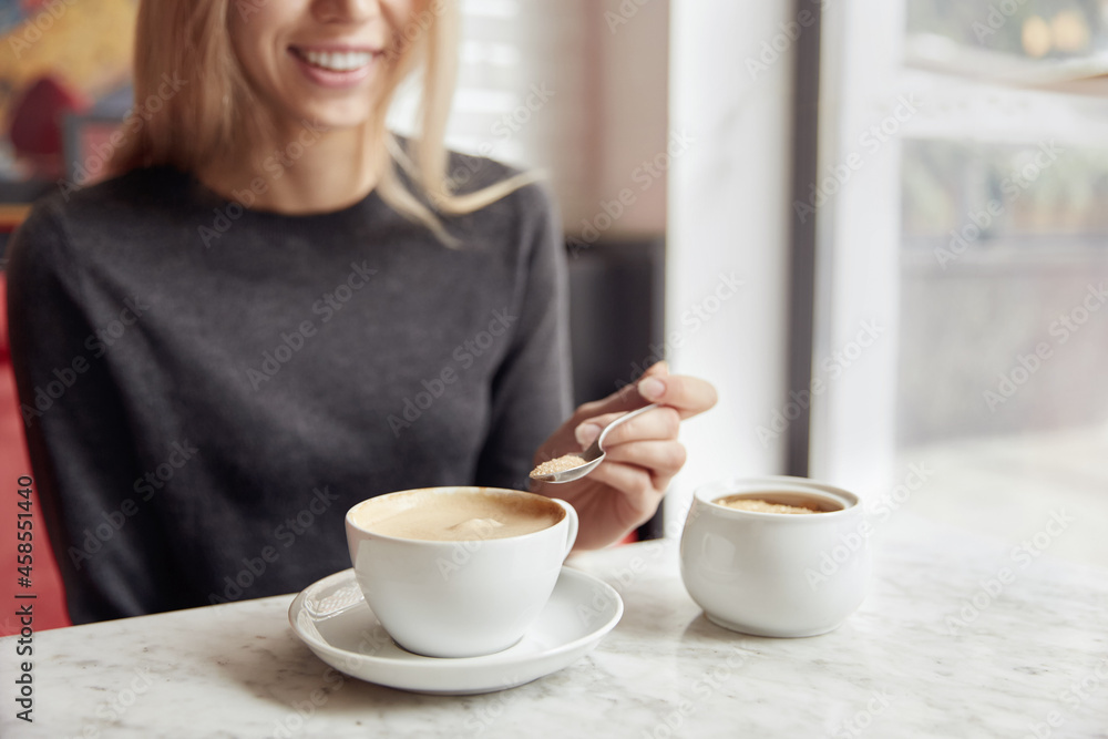Young woman putting sugar in cup with cappuccino Young woman putting sugar in cup with cappuccino