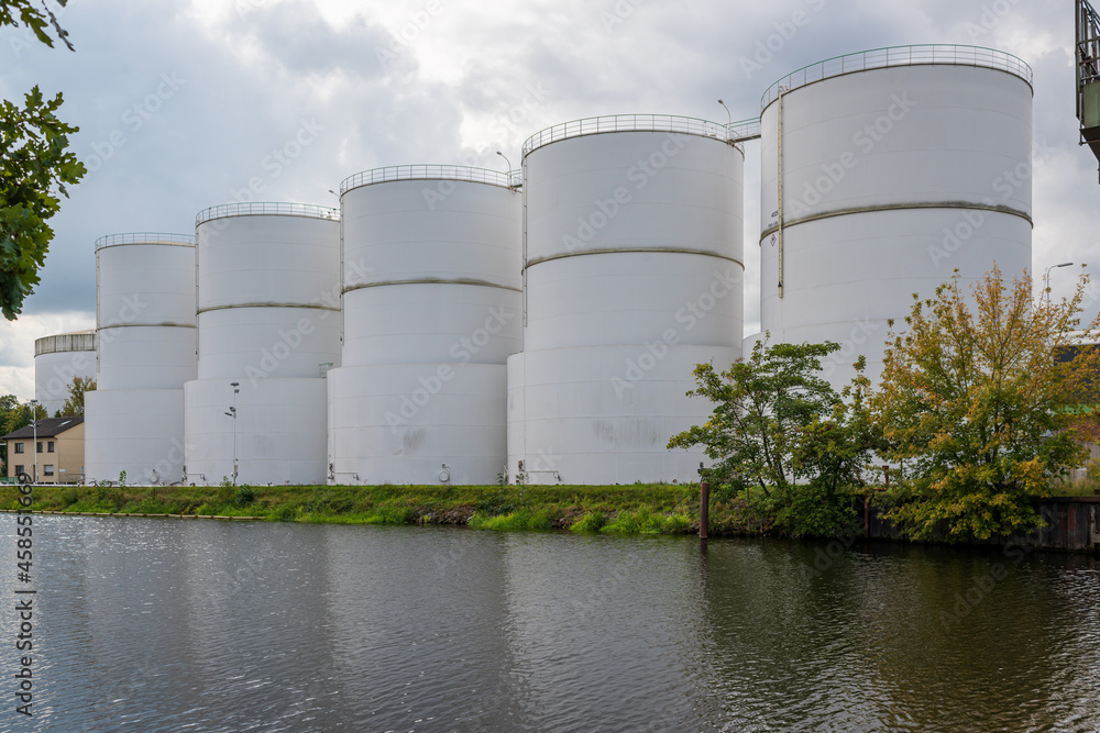 large white steel reservoirs of a tank farm for mineral oil at a canal. large white steel reservoirs of a tank farm for mineral oil at a canal.