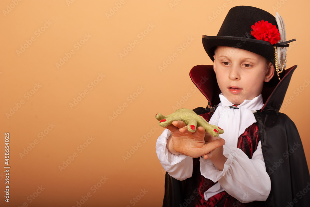 A little boy in a vampire costume with a green hand that lies on his hand on Count Dracula's Halloween on a beige background with space for the text concept of discounts for the shopping center A little boy in a vampire costume with a green hand that lies on his hand on Count Dracula's Halloween on a beige background with space for the text concept of discounts for the shopping center