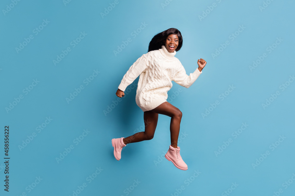 Full length photo of impressed funny dark skin lady wear white winter outfit jumping running isolated blue color background Full length photo of impressed funny dark skin lady wear white winter outfit jumping running isolated blue color background