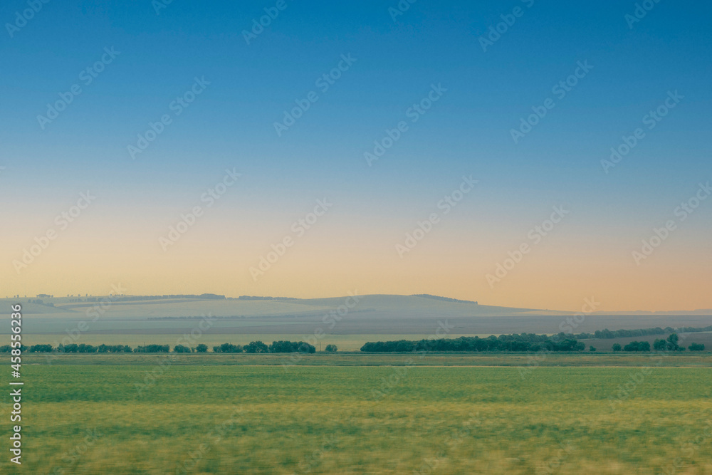 Green field with forest line blur in motion, against the background of sunset