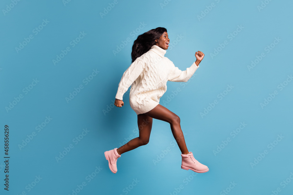 Photo of purposeful dark skin woman dressed white winter clothes running fast isolated blue color background Photo of purposeful dark skin woman dressed white winter clothes running fast isolated blue color background