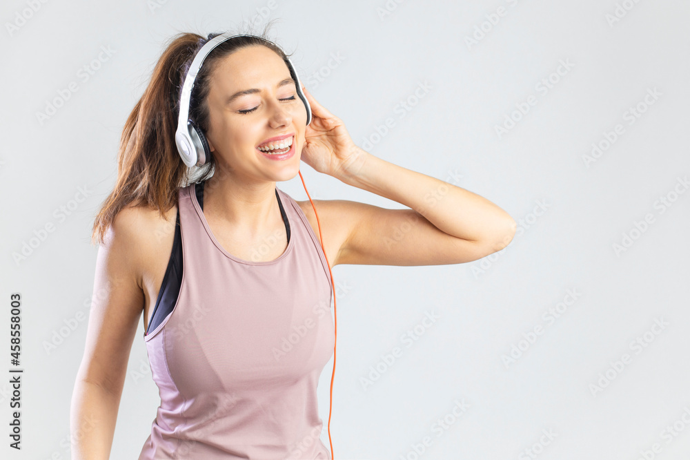 Sporty young woman in headphone holding smartphone and dancing over gray background. Sporty young woman in headphone holding smartphone and dancing over gray background.