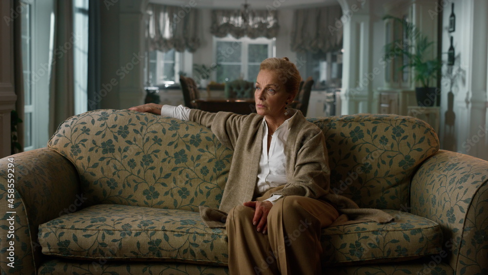 Serious aged woman looking camera luxury home. Senior woman relaxing couch. Serious aged woman looking camera luxury home. Senior woman relaxing couch.