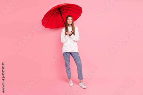 Full size photo of brown hairdo millennial lady with umbrella wear hoodie jeans sneakers isolated on pink background