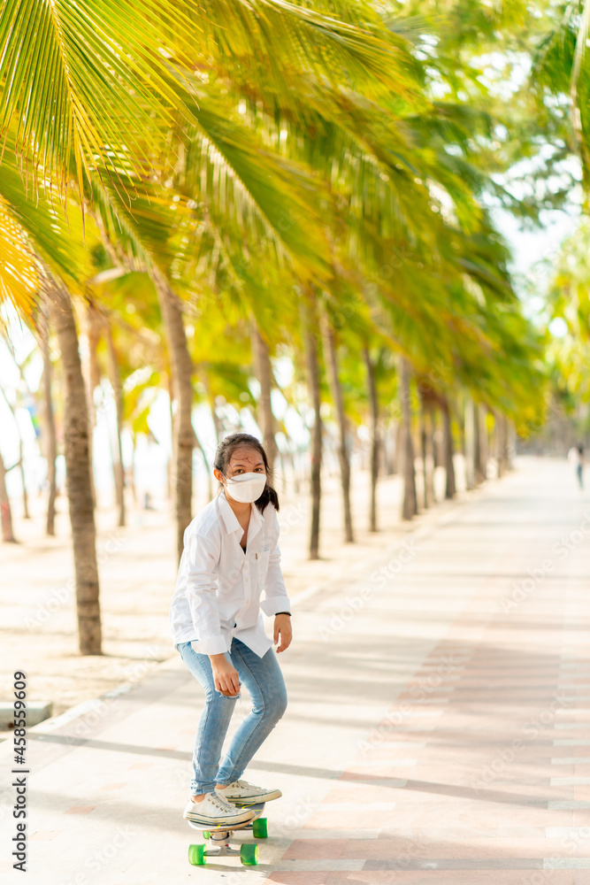 Teen Asian girl in white shirt and jeans is practicing for a play. Surf skating along the beachfront promenade behind many coconut trees, Bangsaen, Thailand.