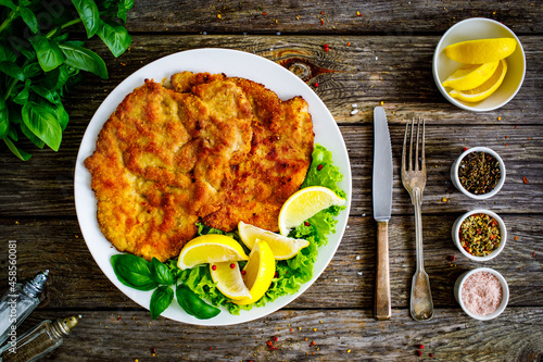 Breaded fried pork chop with lemon and fresh vegetables on wooden table

