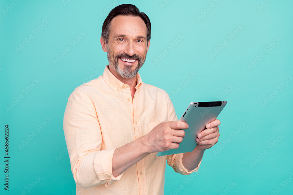 Photo of bossy mature man hold tablet wear peach shirt isolated on teal color background Photo of bossy mature man hold tablet wear peach shirt isolated on teal color background