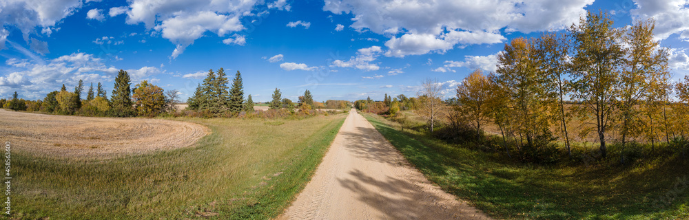 Panoramic view along a country road with autumn colors in the trees and harvested farm fields.

