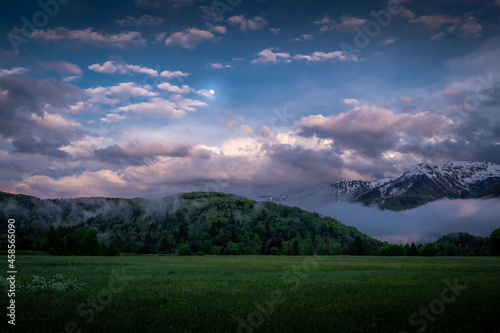 Moonlit landscape with vivid cloud formations and forest at night © Lorant