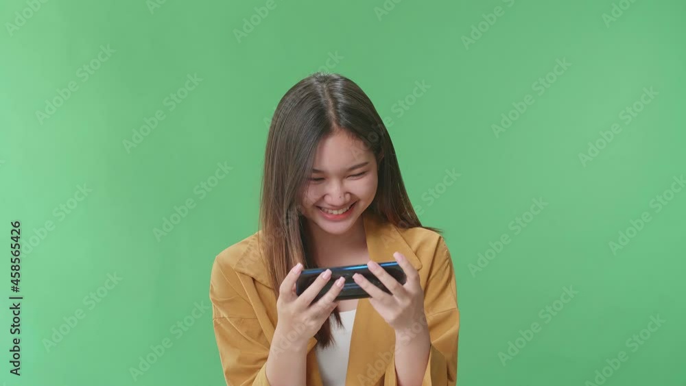 Smiling Asian Woman Looking At The Phone Screen And Holding It In Her Hands While Standing On Green Screen In The Studio
Smiling Asian Woman Looking At The Phone Screen And Holding It In Her Hands While Standing On Green Screen In The Studio