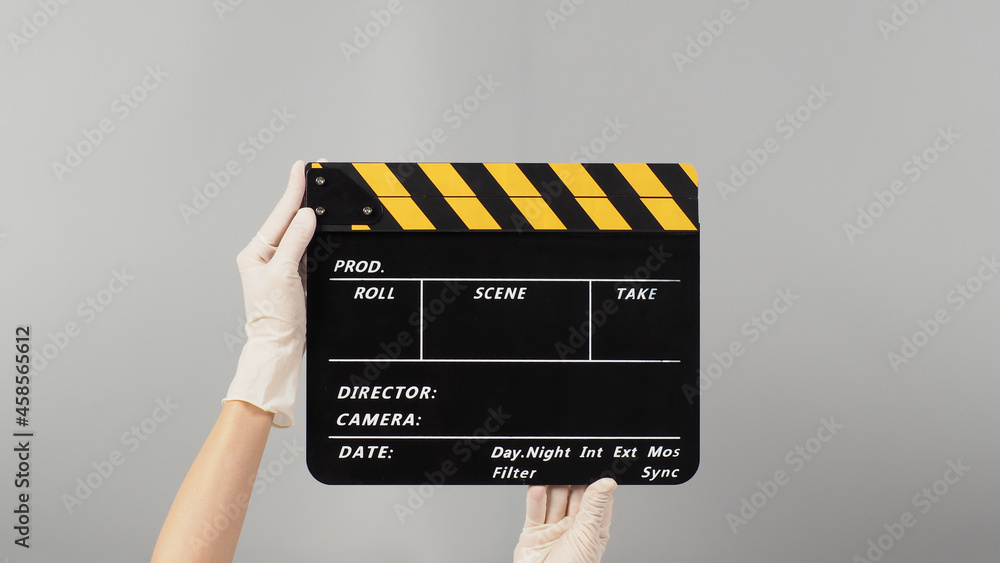 Hand is holding yellow with black clapper board color and wear white medical glove