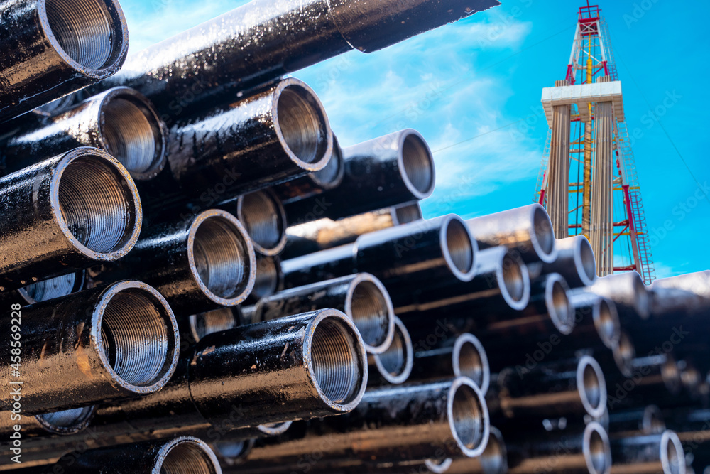 Naklejka premium In the foreground pipes for drilling oil and gas wells. In the background, a blurred image of the rig out of focus. Blue sky with clouds.