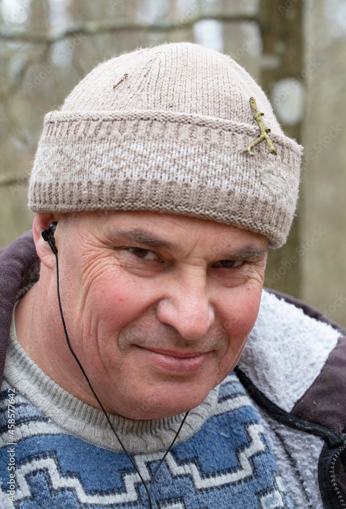 Portrait of a middle-aged man in a knitted hat and warm sweater who listens to music on headphones and looks at the camera. Portrait of a middle-aged man in a knitted hat and warm sweater who listens to music on headphones and looks at the camera.