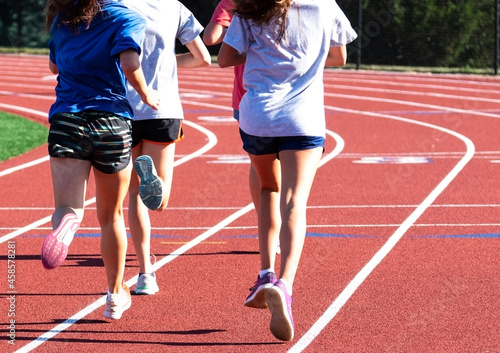 Four girls running fast together on a track from behind