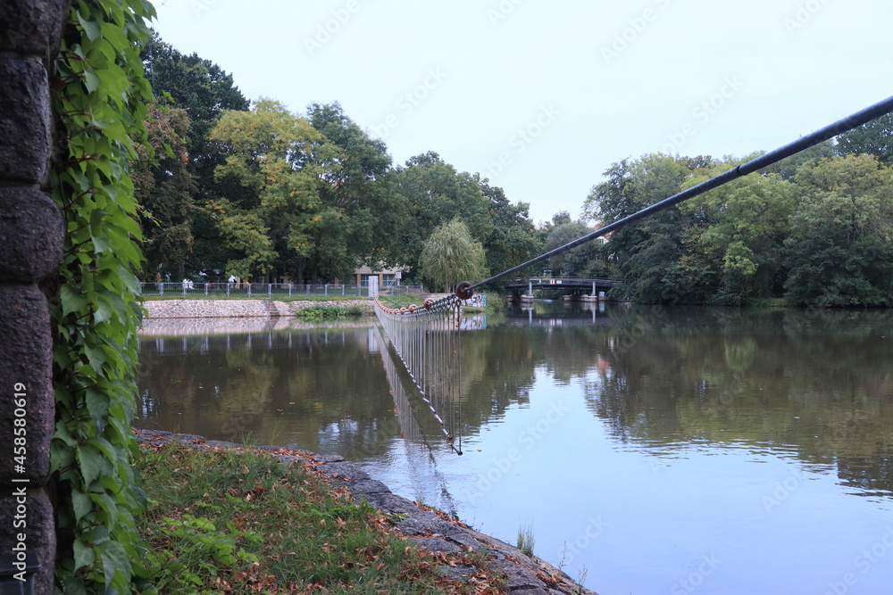 Fototapeta premium Stahlseil-Barriere als Sicherheitseinrichtung auf dem Elsterbecken vor der Wehranlage bei ruhiger Wasseroberfläche, Leipzig, Sachsen, Deutschland