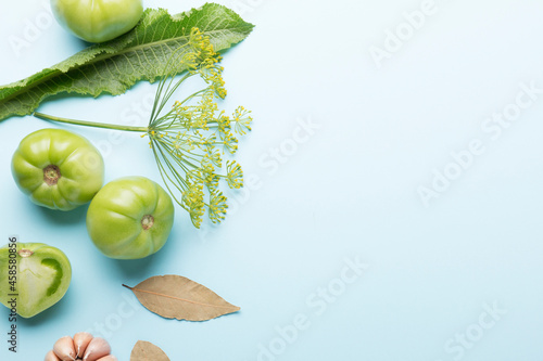 Green tomatoes for canning with spices on a blue background. Unripe tomatoes for harvest. Pepper, garlic, allspice, cloves, horseradish, spices, bay leaf. photo