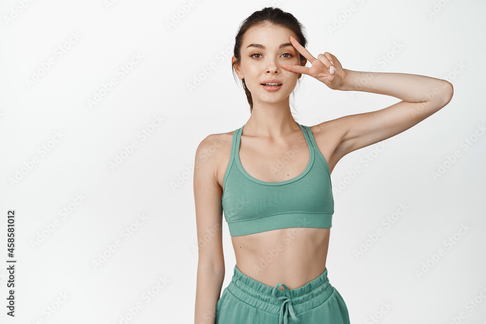 Fitness woman wearing activewear and showing peace, v-sign. Sportswoman looking ready for workout, standing over white background Fitness woman wearing activewear and showing peace, v-sign. Sportswoman looking ready for workout, standing over white background