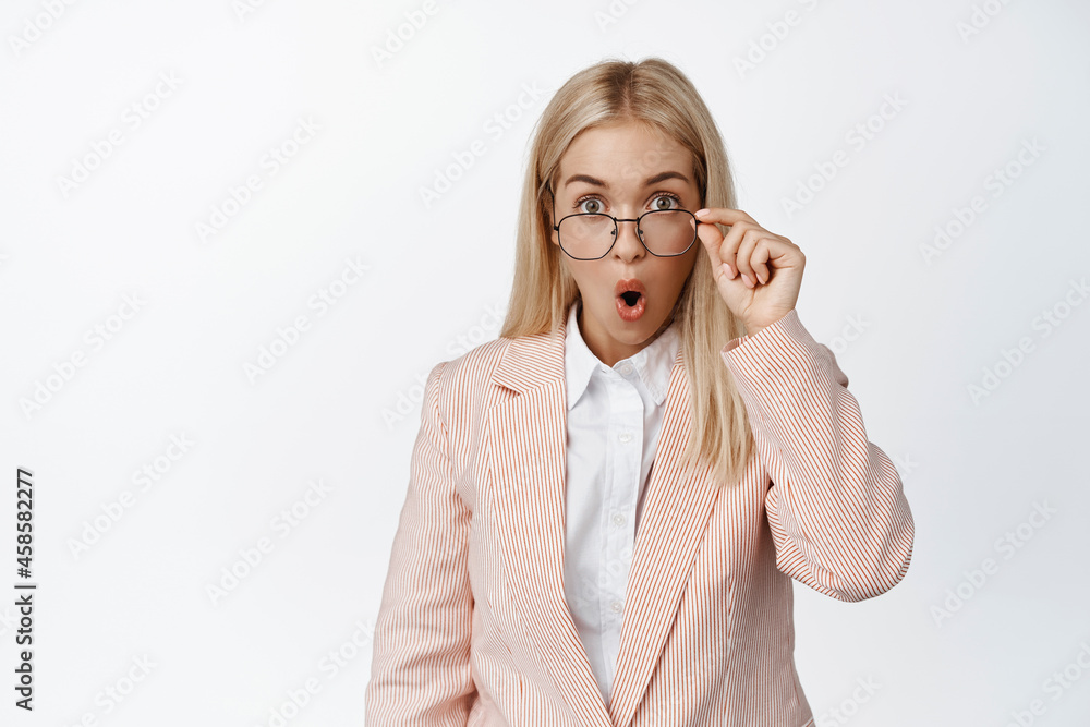 Image of businesswoman looking surprised in glasses, checking out amazing news, standing in pink suit against white background Image of businesswoman looking surprised in glasses, checking out amazing news, standing in pink suit against white background