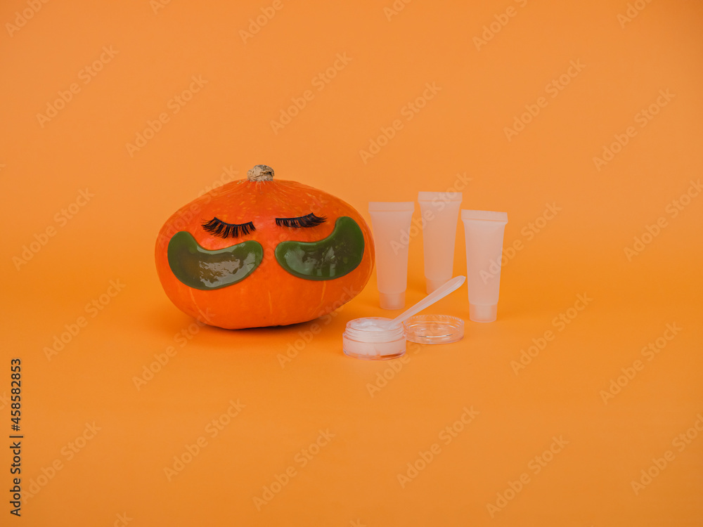 Pumpkin with eye patches on orange background, copy space. Skin care accessories, Halloween.