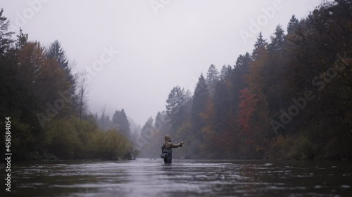 Man standing in the river swinging fishing rod, fly fishing on a autumn rainy day