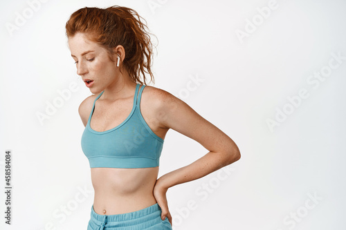 Young redhead sportswoman breathing tired, resting and taking breath after jogging, productive workout training session, standing against white background