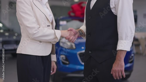 Handshake of Caucasian woman and tattooed man in car dealership in slow motion. Unrecognizable adult dealer and buyer shaking hands indoors in auto showroom making deal. Agreements and commerce photo