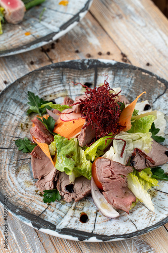 Roast Beef salad with salad leaves and sliced carrot, close up shot on old wooden table