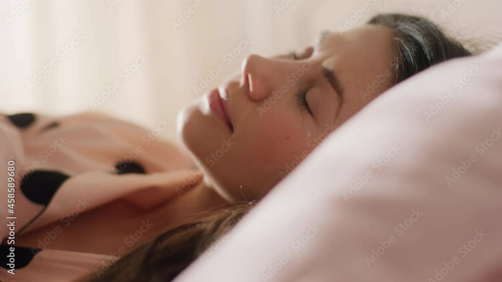 A side shot of a woman fast asleep in the morning while the sun rays beam through the curtains of her room A side shot of a woman fast asleep in the morning while the sun rays beam through the curtains of her room