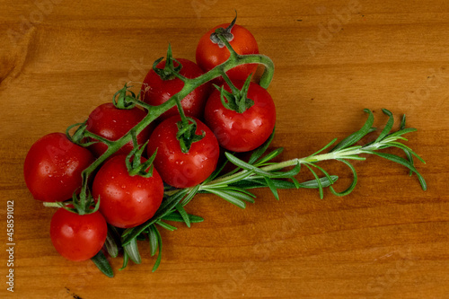 baby fresh red tomatoes  arranged sideways with green branches  fine herbs on the side on the wooden table  photo from above  space for text