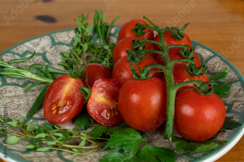 cherry tomatoes on wooden table over white plate with olive oil with herbs. light background, close-up photo