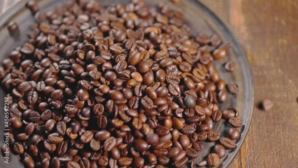 Black coffee beans falling into a pile of coffee in bowl, wooden background Black coffee beans falling into a pile of coffee in bowl, wooden background