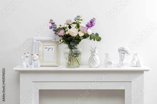 Bouquet of hackelia velutina, purple and white roses, small tea roses, matthiola incana and blue iris in glass vase is on the white coffee table . Grey wall
