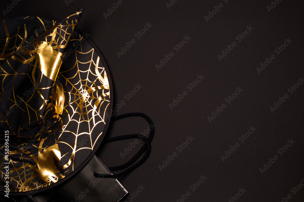 Halloween shopping holiday. Black witch hat with spider web and spider pattern, shopping bag on black background, flat lay. Copy space. - obrazy, fototapety, plakaty 