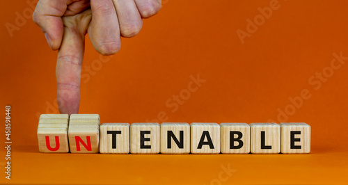Tenable or untenable symbol. Businessman turns cubes and changes the word 'untenable' to 'tenable'. Beautiful orange table, orange background. Business, tenable or untenable concept, copy space. photo