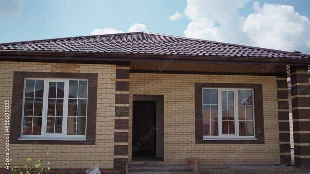 Construction of a private house. Unfinished one-storey house. The roof is made of metal tiles. Slow motion. Construction of a private house. Unfinished one-storey house. The roof is made of metal tiles. Slow motion.
