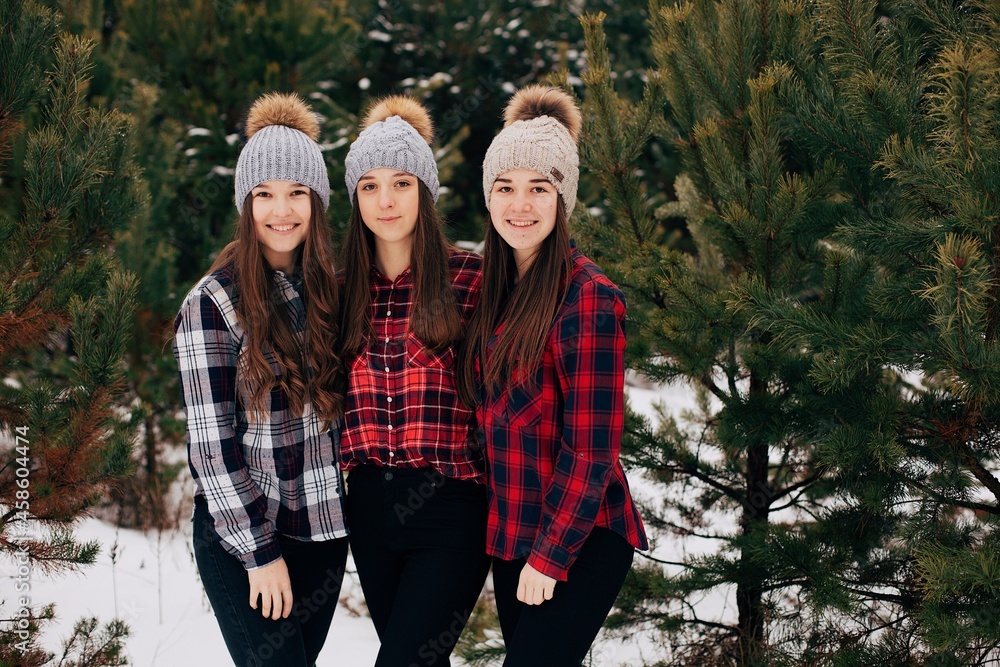 three girls in checkered shirts in the winter forest. Three sisters in winter hats and plaid shirts three girls in checkered shirts in the winter forest. Three sisters in winter hats and plaid shirts