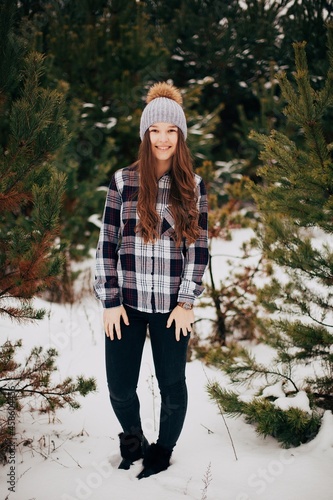 Portrait of a beautiful girl with long hair in a snowy forest. Winter in the woods. Girl walks in the winter forest. Checkered shirt. Cold winter day. Beautiful pines in the snow