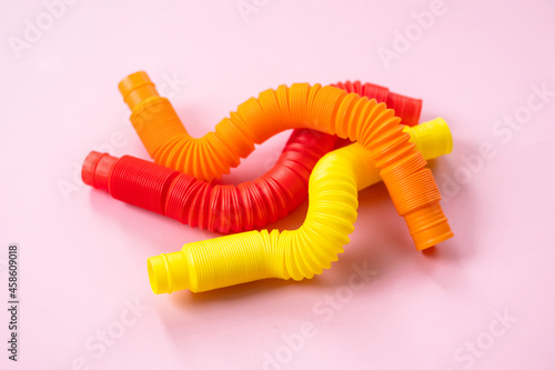 Colorful anti-stress fidget push pop tube sensory toys for children on pink background. Top view  flat lay. Close-up of creative game with popular plastic flexible bright corrugated pipe.