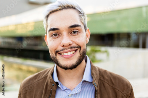Young hispanic man smiling on camera outdoors - Portrait of happy trendy guy in the city - Millennial people concept