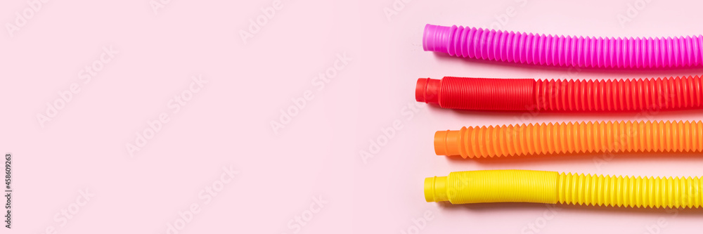 Colorful anti-stress fidget push pop tube sensory toys for children on pink background. Top view, flat lay. Close-up of creative game with popular plastic flexible bright corrugated pipe. Banner - obrazy, fototapety, plakaty 