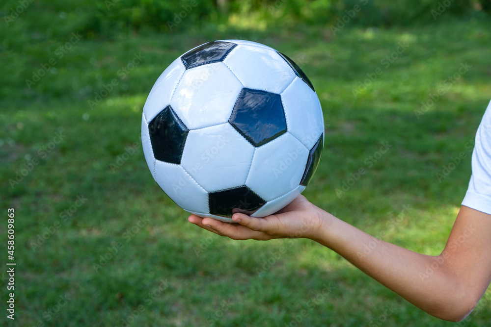 Soccer ball white and black leather in hand of football player on green grass.