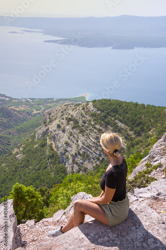 A girl sits on the edge of a cliff and looks at the sea