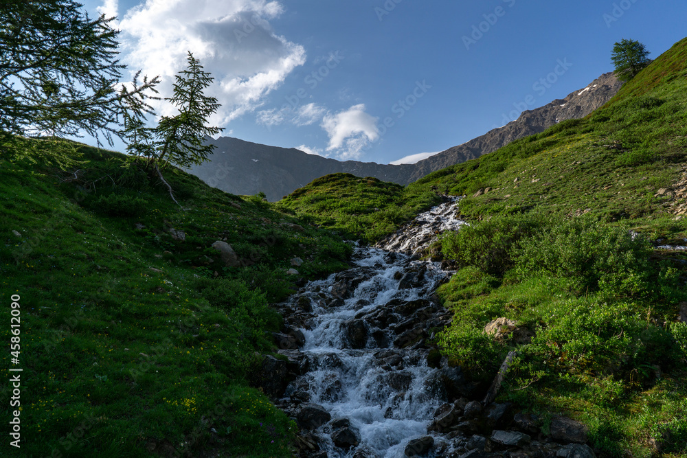 View of relaxing mountain scenery with mountains in the background. Meadow, grass and stream of water as part of the landscape