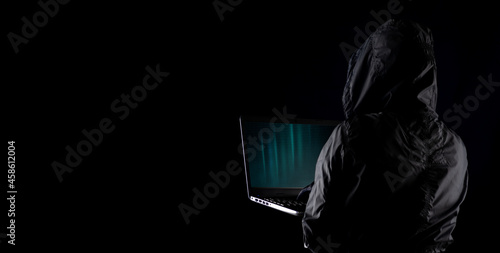 Fototapeta Naklejka Na Ścianę i Meble -  Hooded cybercriminal hacker using laptop to hack internet in cyberspace but black background, internet personal data security concept