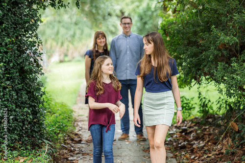 A family of a mother and father and two daughters taking a walk in the neighborhood on the sidewalk outside in the summer