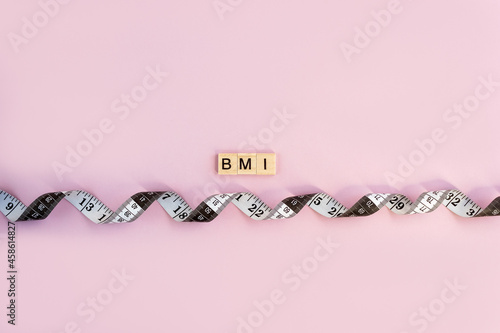 Word BMI on wooden blocks with lettering and measuring tape on pastel background. Control concept Body Mass Index. Copy space