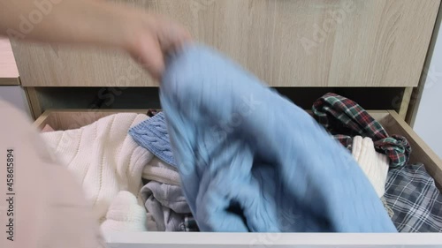 Woman hands trying to find the right thing in a drawer with clothes in a mess, disorder in house and clothes, decluttering needed